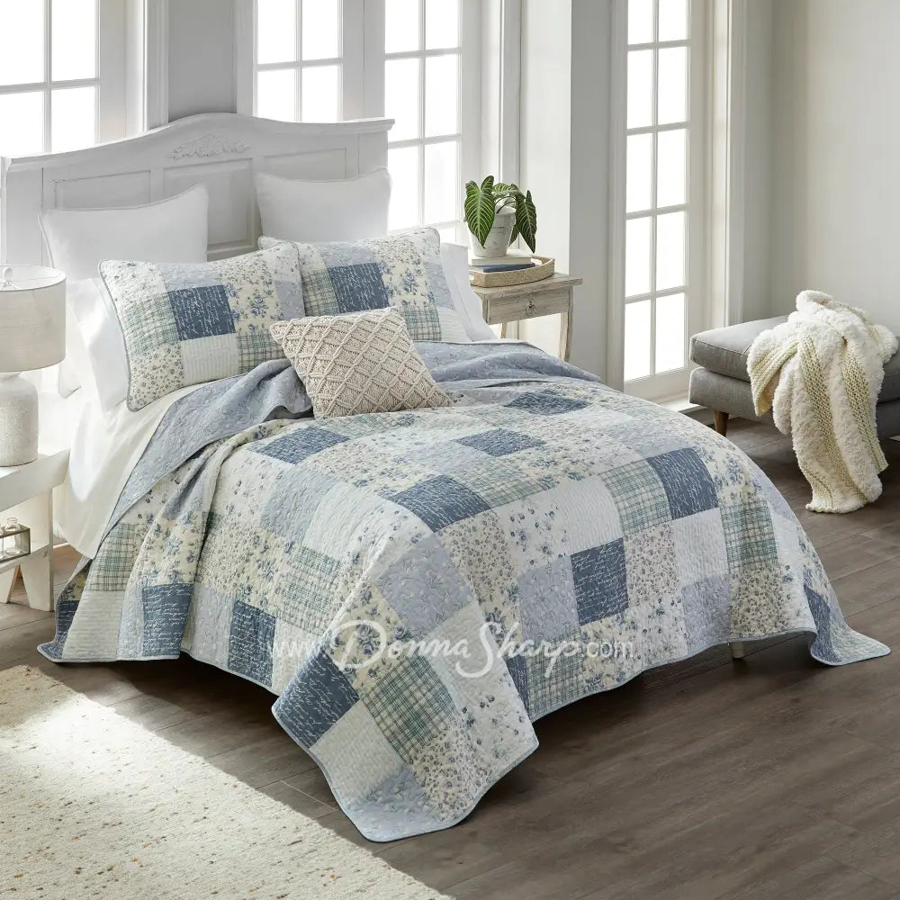 Donna Sharp Blue Pastures cotton patchwork quilt set styled on bed in coastal farmhouse bedroom with soft blues, gentle creams, and crisp white floral and plaid blocks
