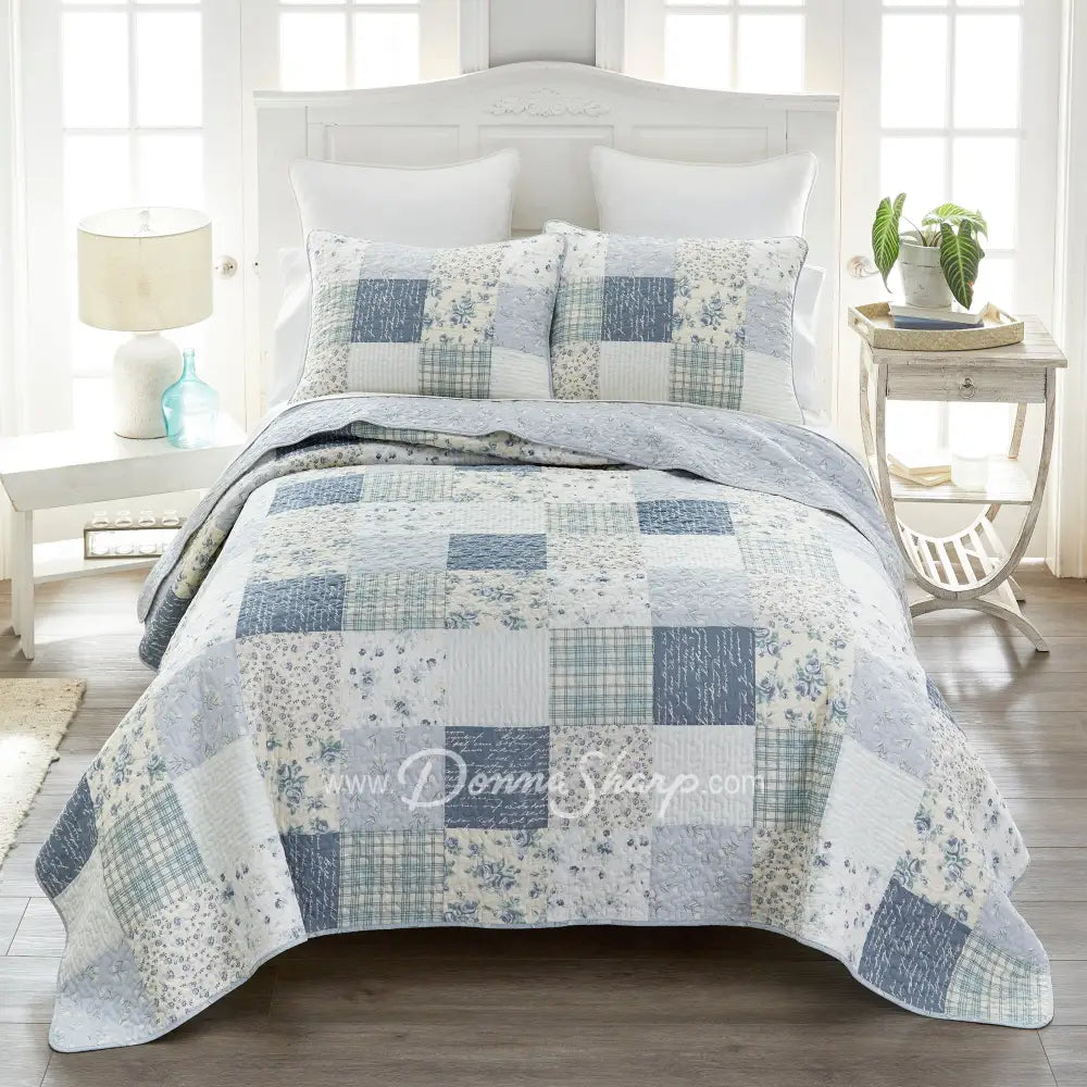Donna Sharp Blue Pastures cotton patchwork quilt set styled on bed in coastal farmhouse bedroom with soft blues, gentle creams, and crisp white floral and plaid blocks