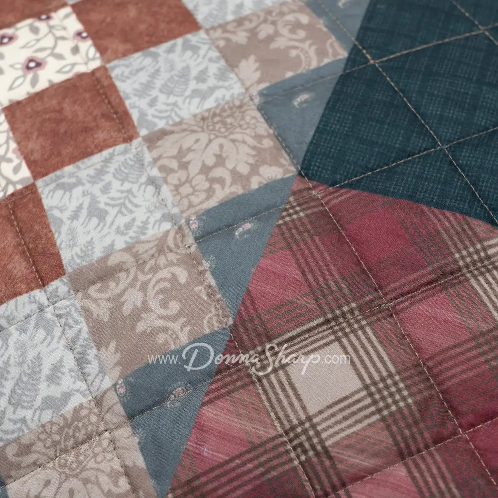 Close-up of Donna Sharp Greenwood Patch quilt showing patchwork blocks with greens ranging from sage to deep olive, warm browns, muted terracotta, hints of denim and spruce blue, and aged parchment ivories and tans and pine cone patterns with diamond quilting stitches