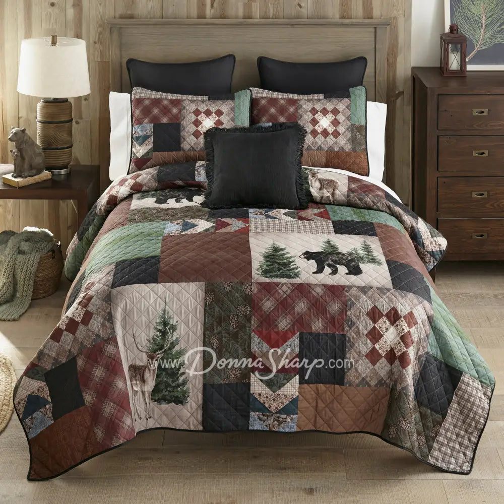 Donna Sharp Greenwood Patch quilt set styled on bed in rustic lodge bedroom with bear, deer and pine tree appliques in sage, deep olive, warm browns, muted terracotta, hints of denim and spruce blue, and aged parchment ivories and tans patchwork