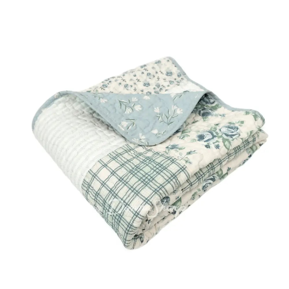 Donna Sharp Blue Pastures reversible cotton throw blanket folded to show patchwork patterns in blue, gray and cream with floral, plaid and script fabrics