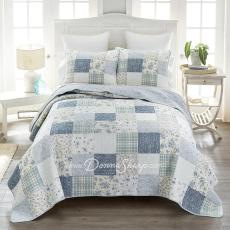 Donna Sharp Blue Pastures cotton patchwork quilt set styled on bed in coastal farmhouse bedroom with soft blues, gentle creams, and crisp white floral and plaid blocks