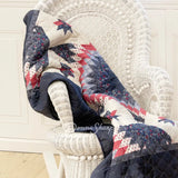 Donna Sharp Bluefield Star reversible throw blanket draped on white wicker chair showing a floral star pattern with navy, country blue, periwinkle, pale ivory, rose, and raspberry, with a solid navy reverse side