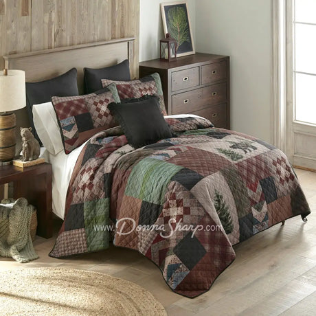 Donna Sharp Greenwood Patch quilt set styled on bed in rustic lodge bedroom with bear, deer and pine tree appliques in sage, deep olive, warm browns, muted terracotta, hints of denim and spruce blue, and aged parchment ivories and tans patchwork