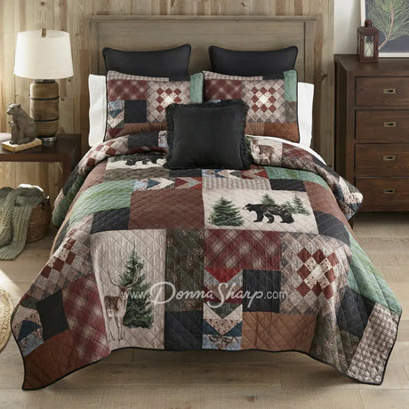 Donna Sharp Greenwood Patch quilt set styled on bed in rustic lodge bedroom with bear, deer and pine tree appliques in sage, deep olive, warm browns, muted terracotta, hints of denim and spruce blue, and aged parchment ivories and tans patchwork