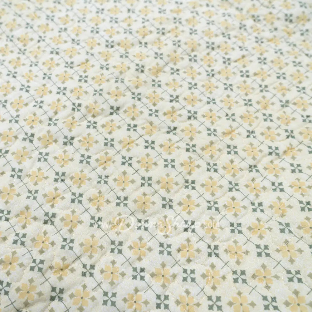 Close-up of Donna Sharp Meadow cotton quilt fabric showing cream background with yellow floral clusters and sage green geometric lattice pattern