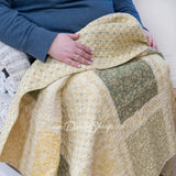 Person wrapped in Donna Sharp Meadow cotton patchwork lap blanket showing soft texture and soothing shades of sage green, beige, white, buttercream gold, and cream floral patterns